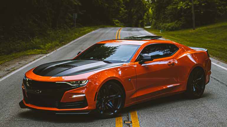 orange and black LS Camaro parked on street surrounded by trees